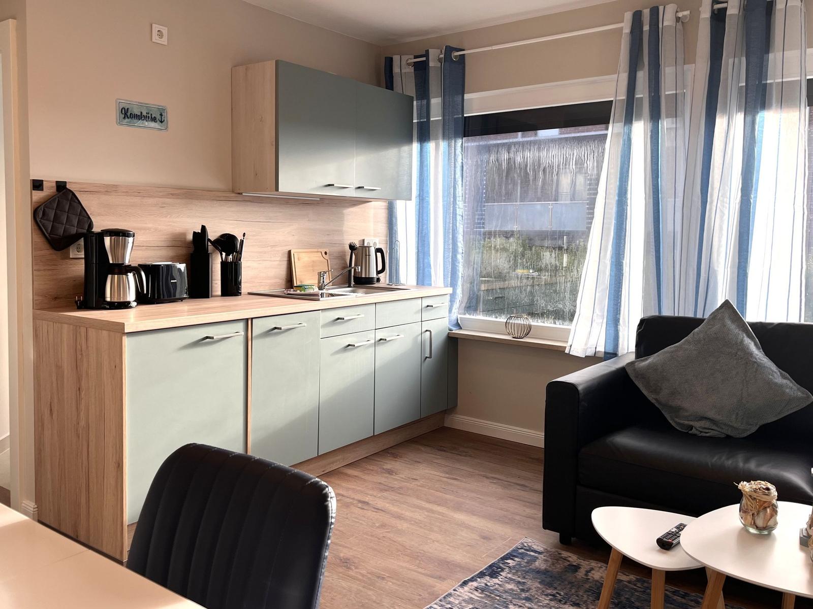 Küche mit Arbeitsfläche, Spüle und Küchenzeile. Wohnbereich mit Sofa und Fenster.