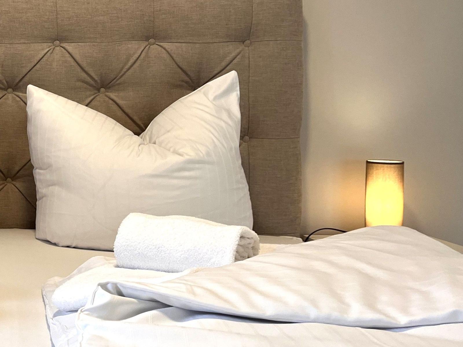 Bettkopfteil mit Knopfstickerei, zwei Kissen, eine Decke und eine Lampe.