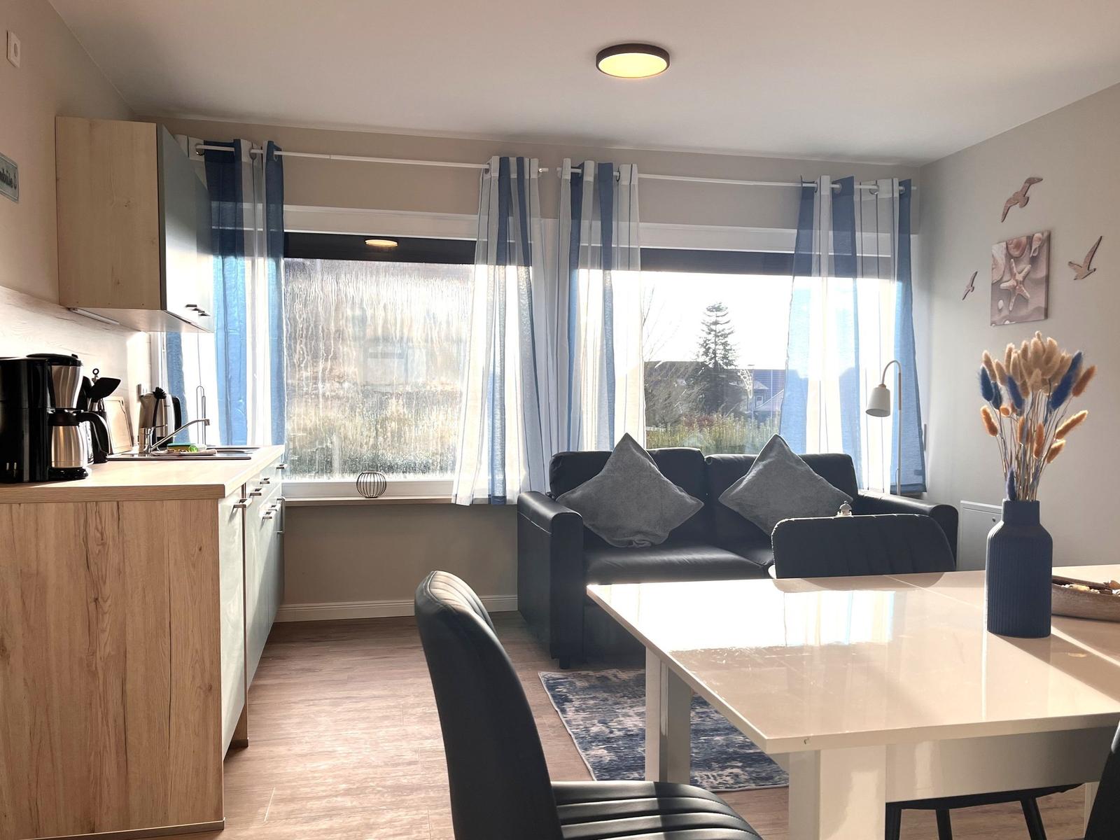 Wohnküche mit Essbereich, Sofa und Fenster mit blauen Vorhängen.