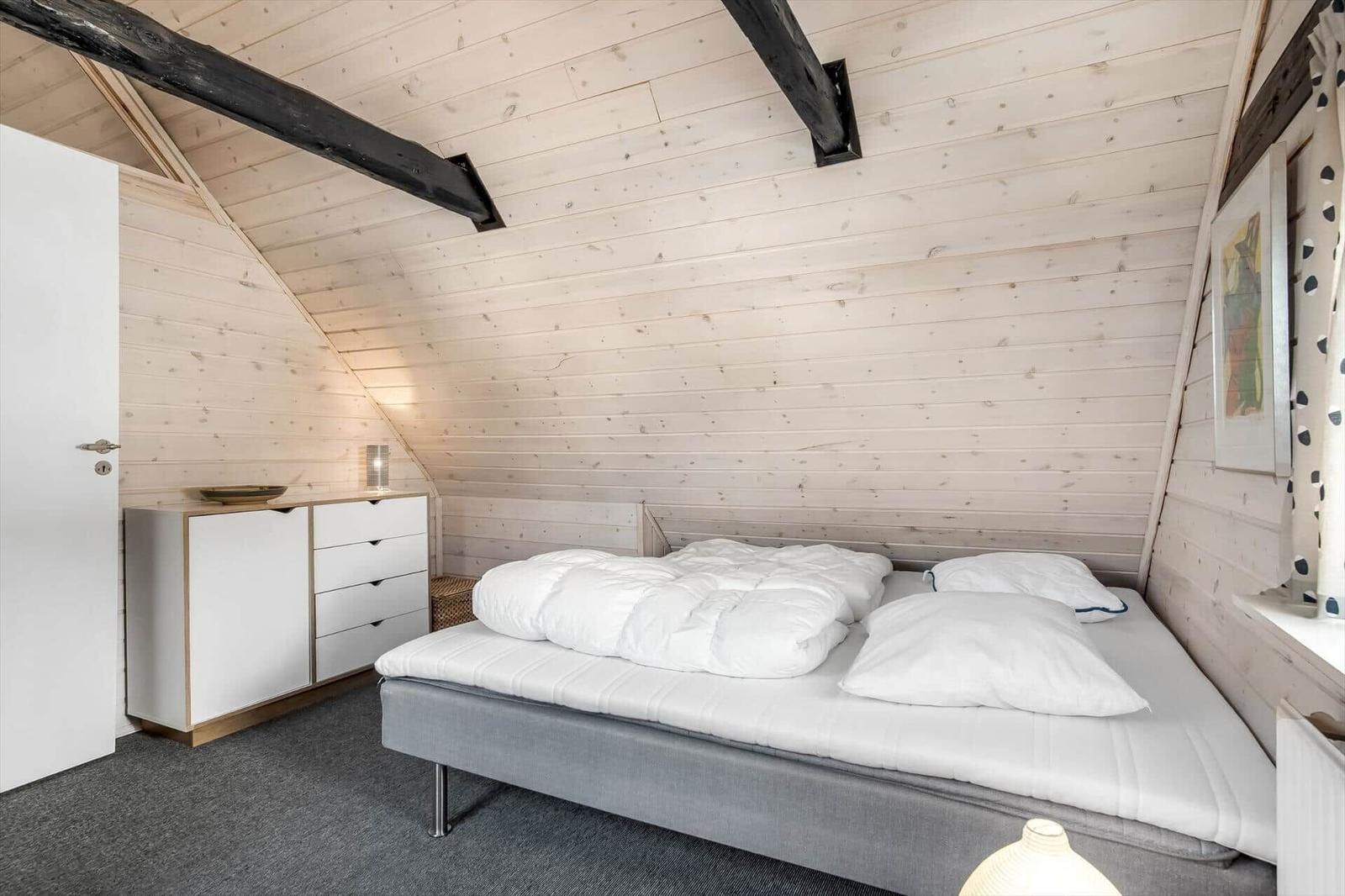 Bedroom with sloped ceiling, bed, dresser, and wood walls