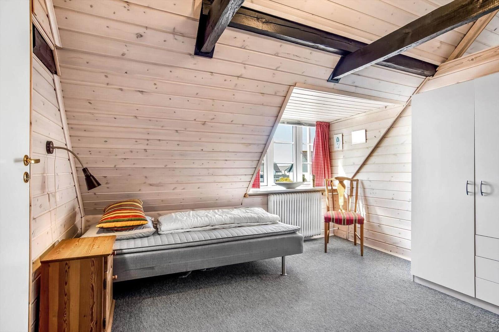 Bedroom with wooden walls, bed, chair, and wardrobe under sloped ceilings.