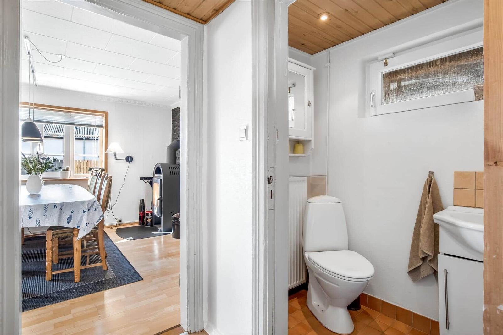 Bathroom with toilet and sink. In the background, the dining room with table and chairs is visible.