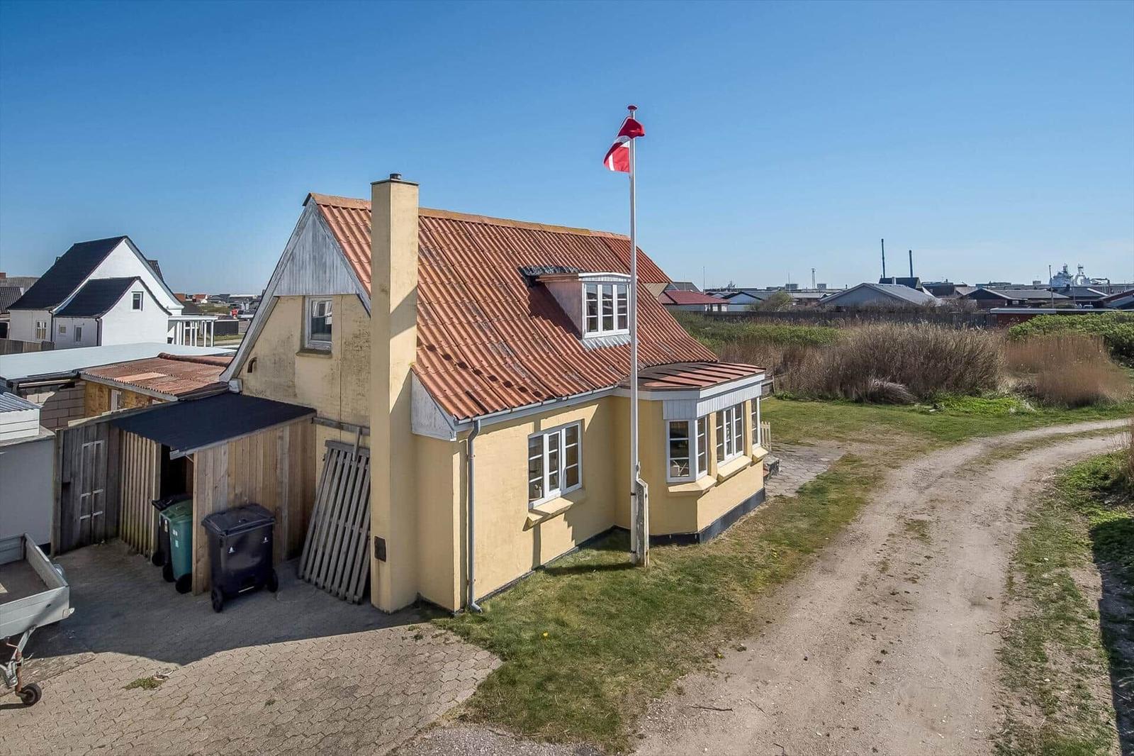 Yellow house with red roof and Danish flag. Surrounded by grass and an unpaved path.