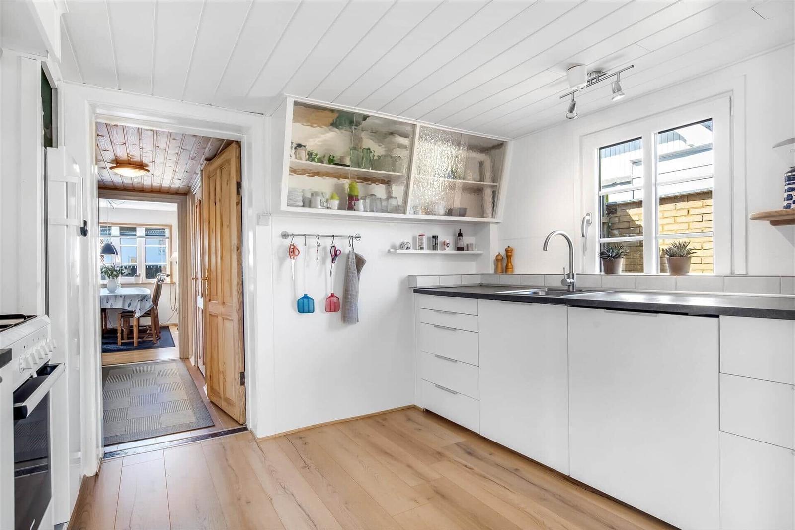 Kitchen with white cabinets, wooden floor, and window. Passage to dining area.