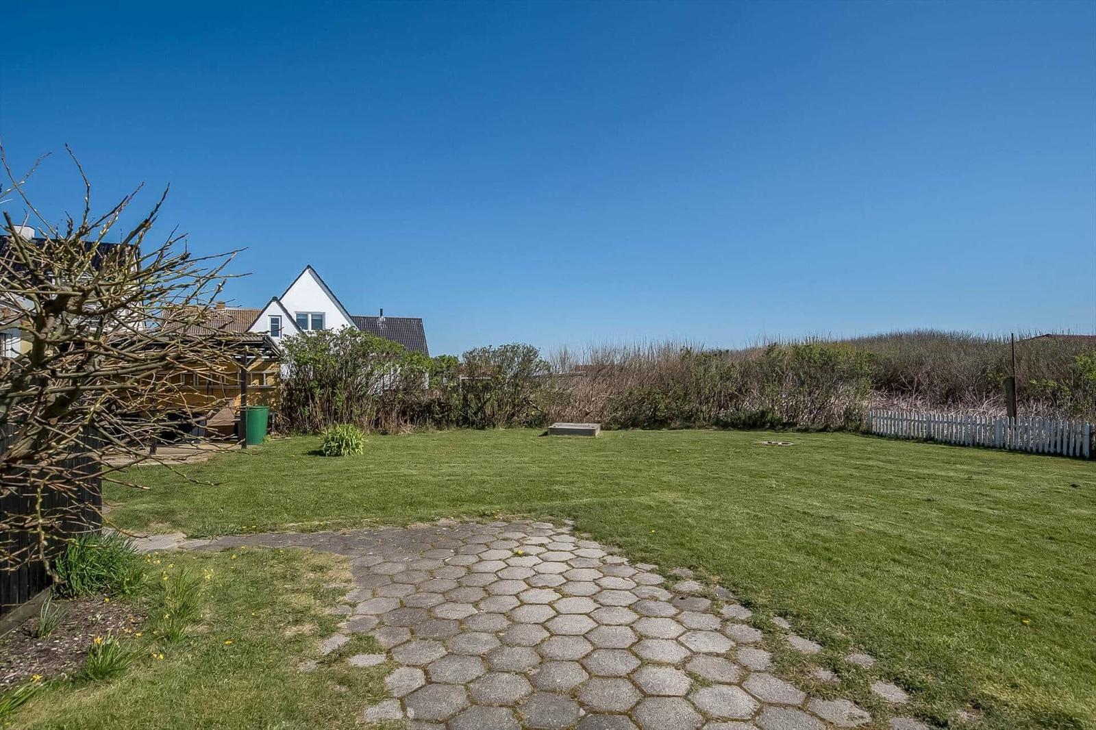 Backyard with grass area, stone path, and white fence.