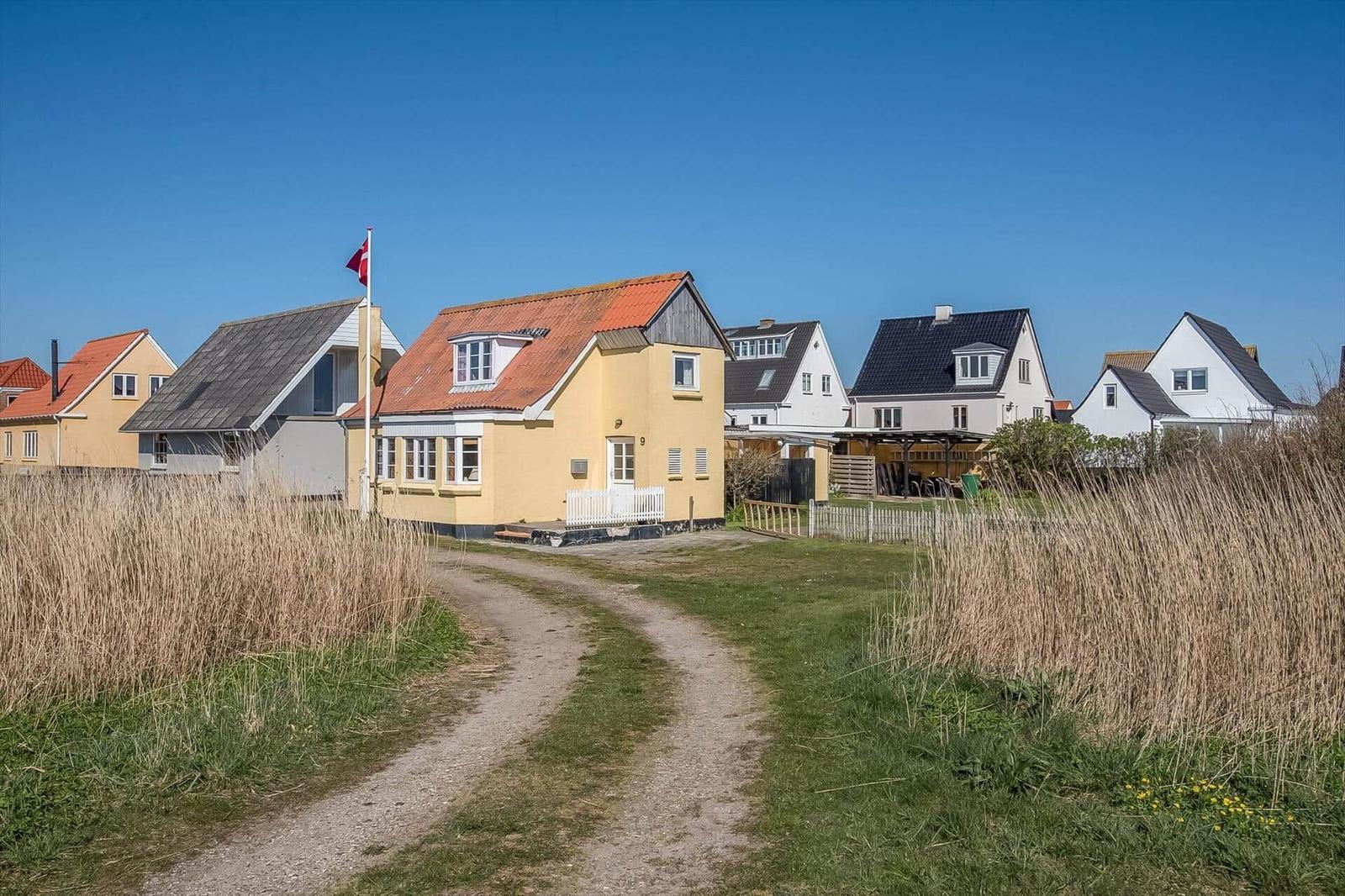 Yellow house with red roof and white windows. Other houses are behind it.