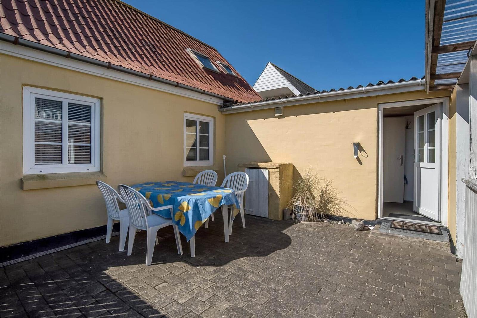 Backyard with table, chairs, and entrance door. Yellow walls and red roof.