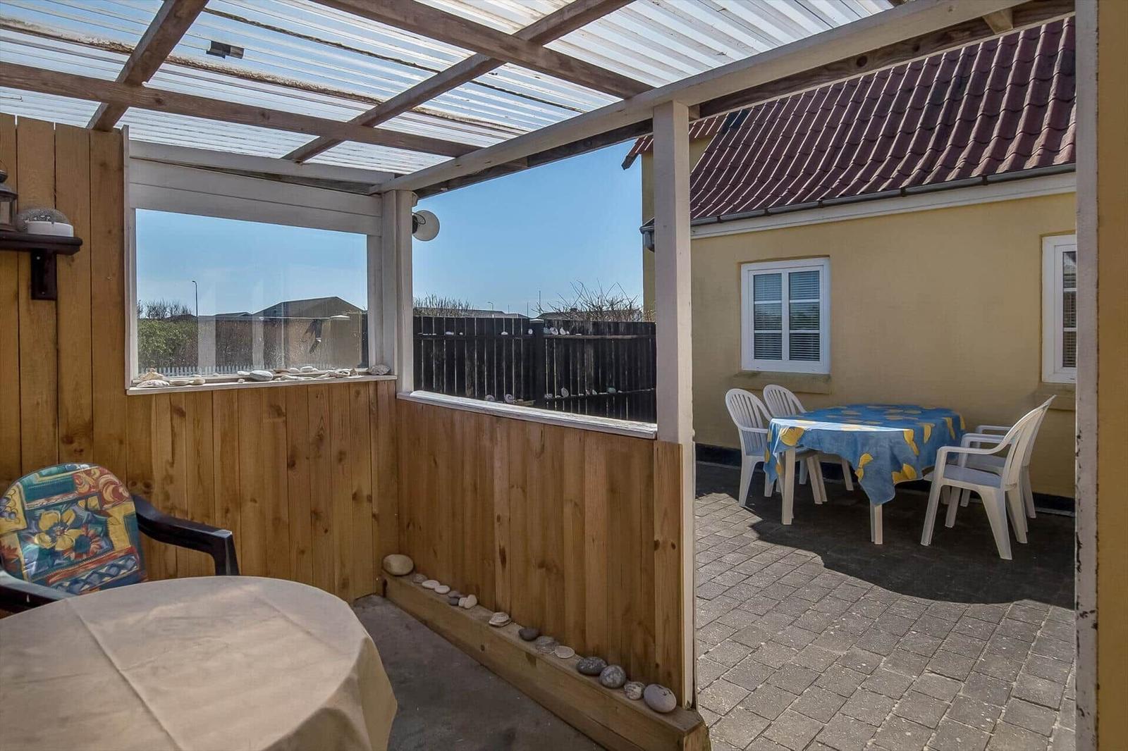 Terrace with table, chairs, and view of yellow house with roof.