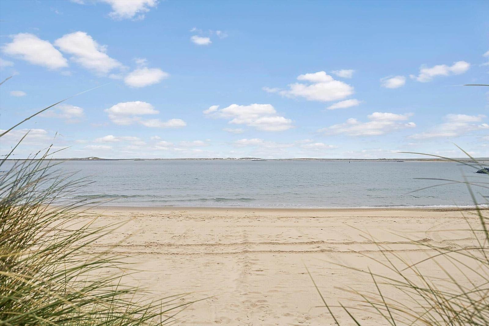 Beach with sand and gentle waves under blue sky with white clouds.