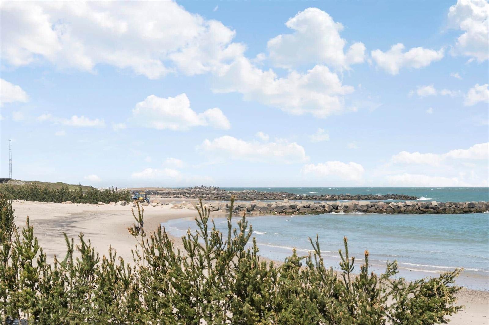Beach with rock breakwater and green vegetation under blue sky with white clouds.