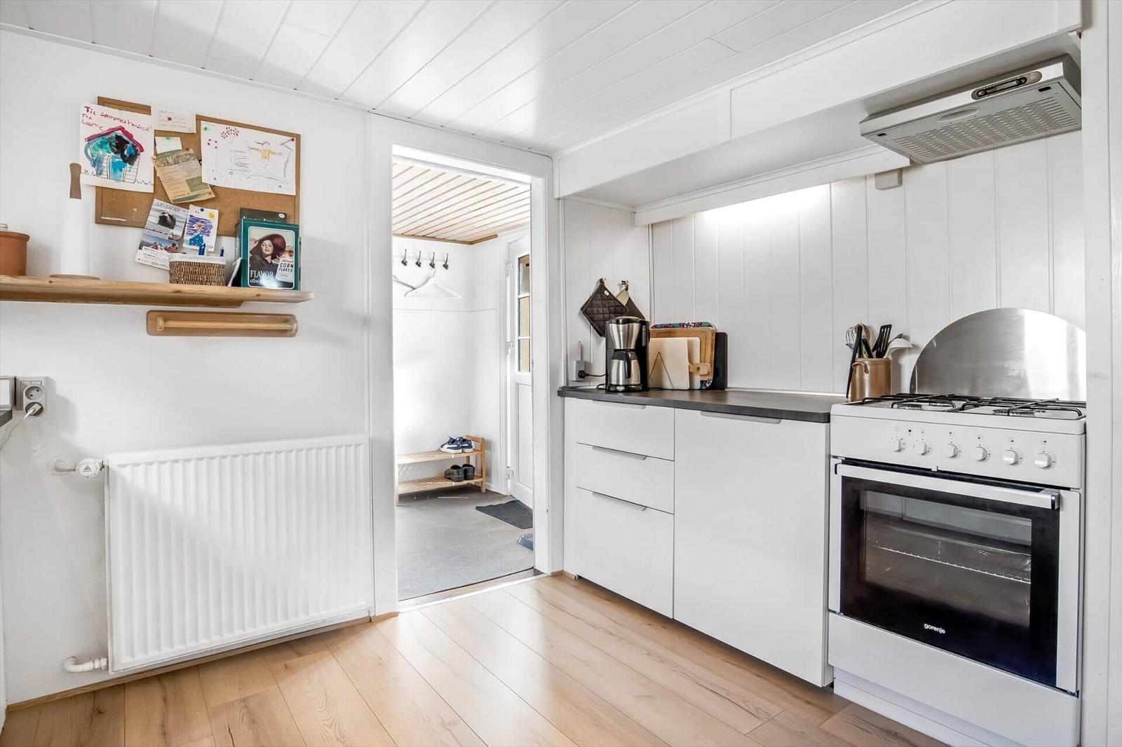 Kitchen with white cabinets, stove, and exhaust hood. Passage to another room.