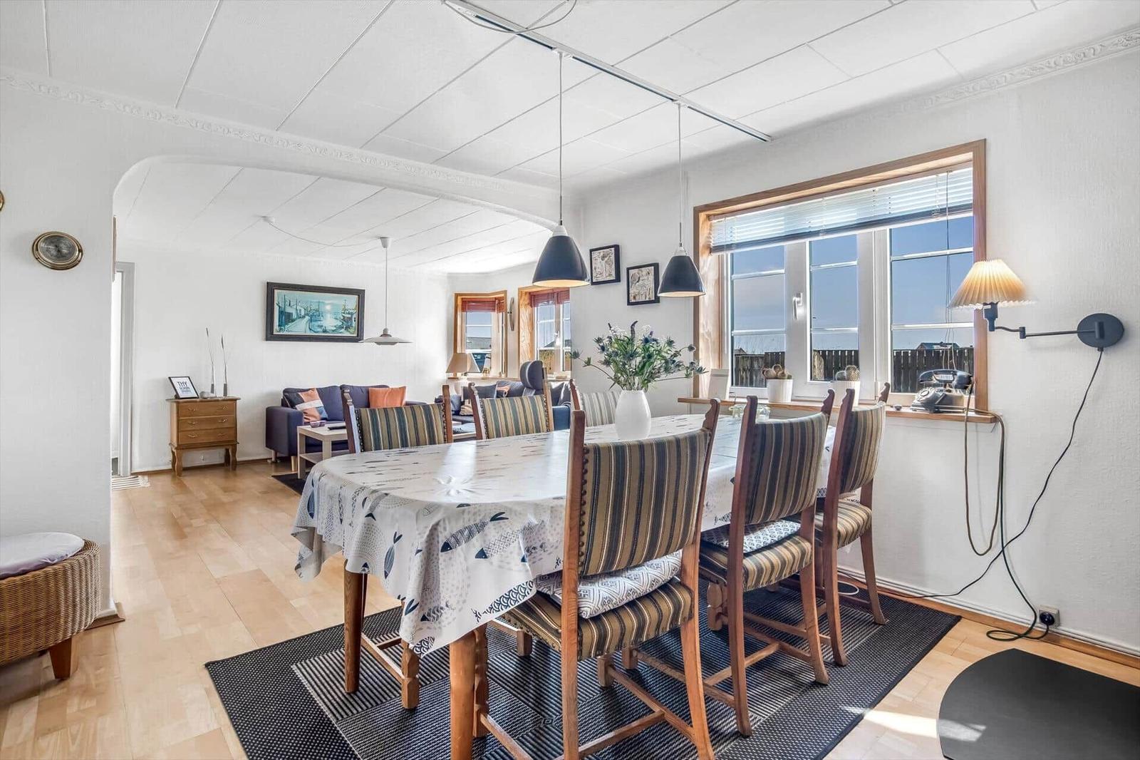 Dining room with table and chairs, view into living room with sofa and windows.