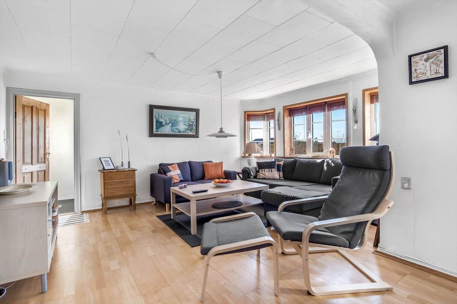 Living room with sofa, chair and wooden floor. Windows with view outside.