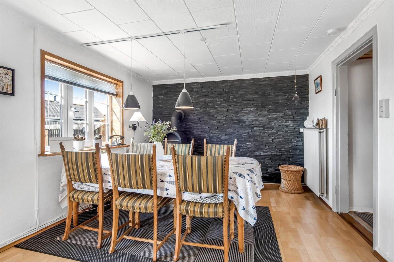 Dining room with wooden table, striped chairs, and stone wall in background.