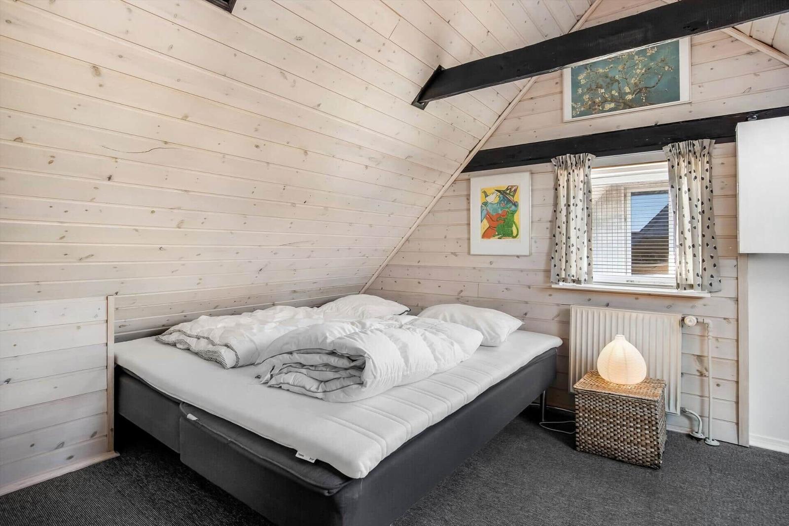 Bedroom with wooden walls, bed, window, and bedside table.