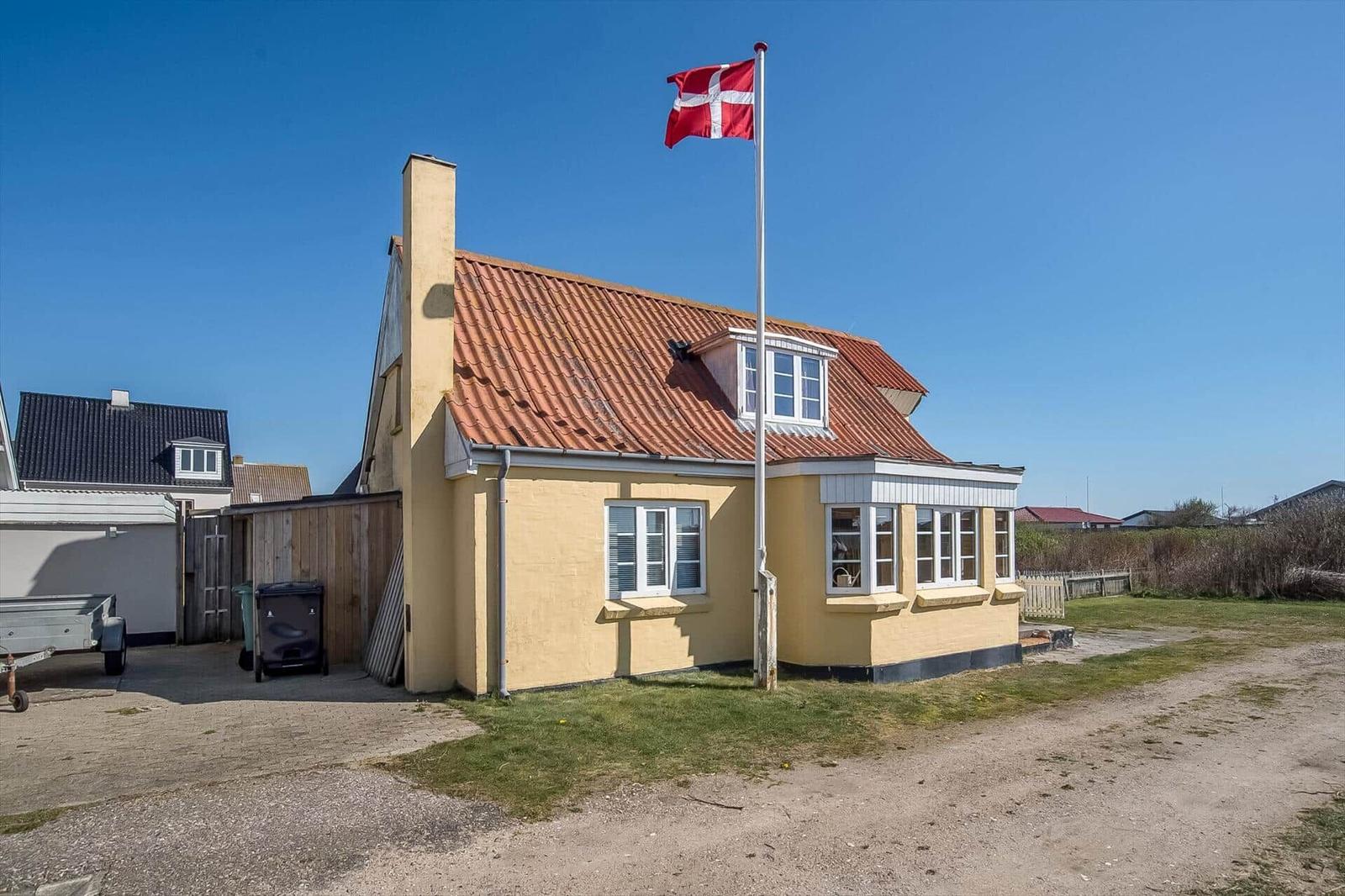 A yellow house with a red roof and a Danish flag in the foreground.