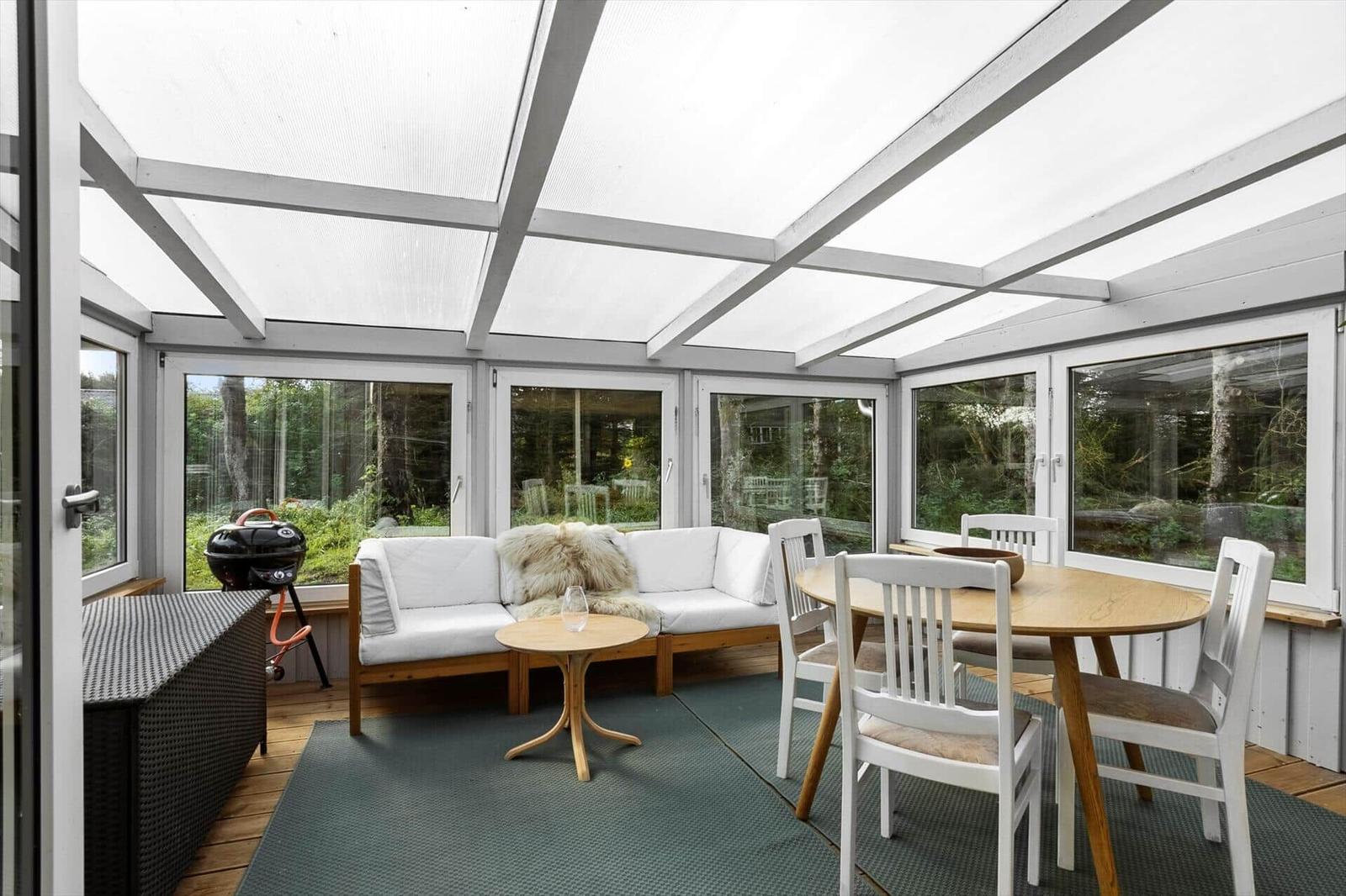 Terrace with seating, dining table, and grill. Fully glazed with garden view.