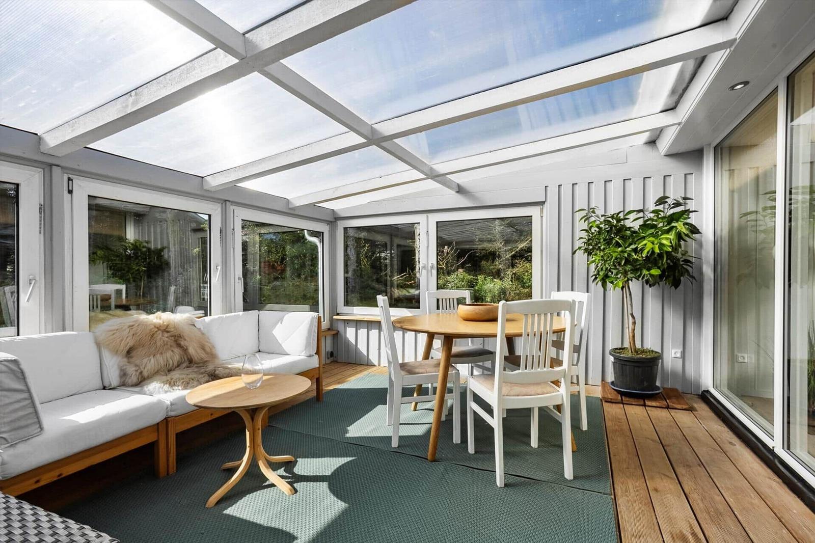 Terrace with seating area, dining table, and plant under glass roof.