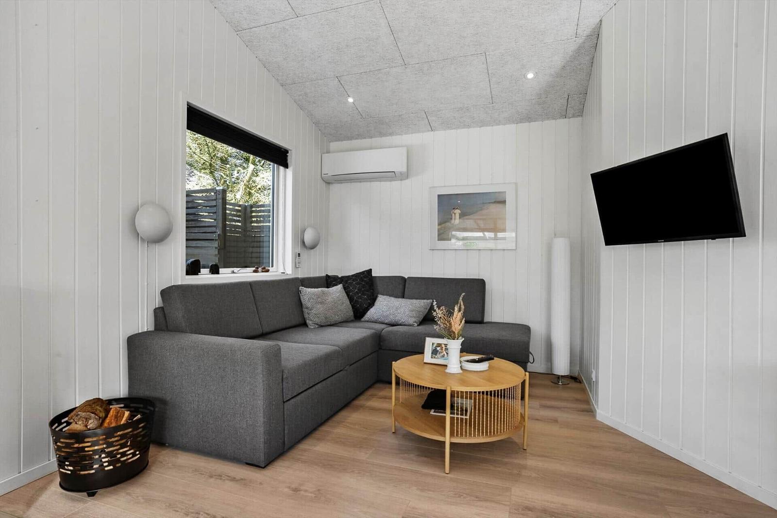 A living room with gray sofa, round table, and wall-mounted TV.