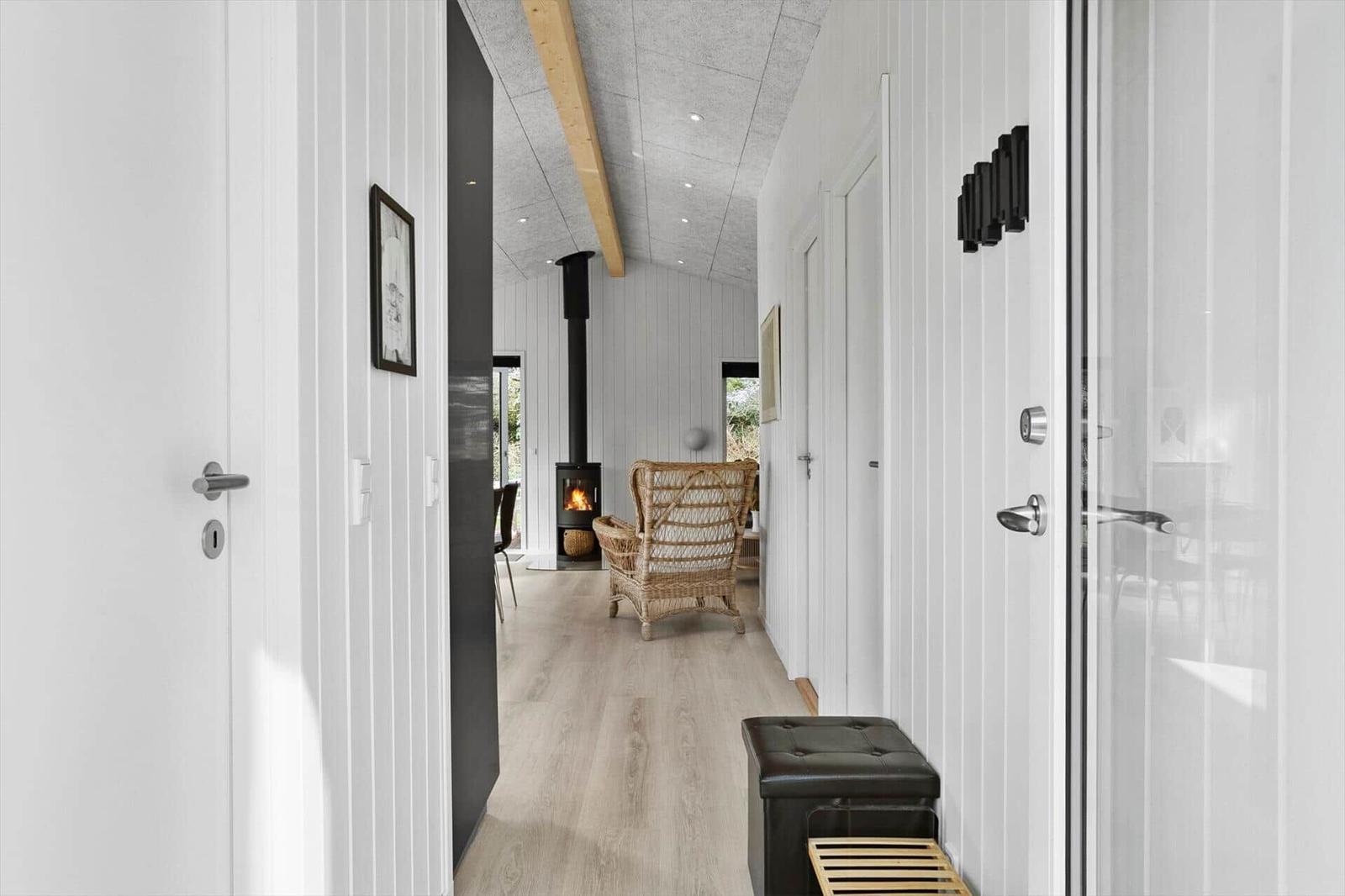 Hallway with wooden floor, white walls, seating area, and fireplace in the background.