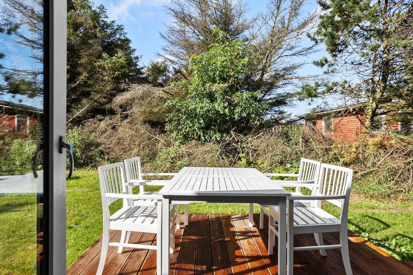 Bright terrace with white table and chairs. Greenery and trees in the background.