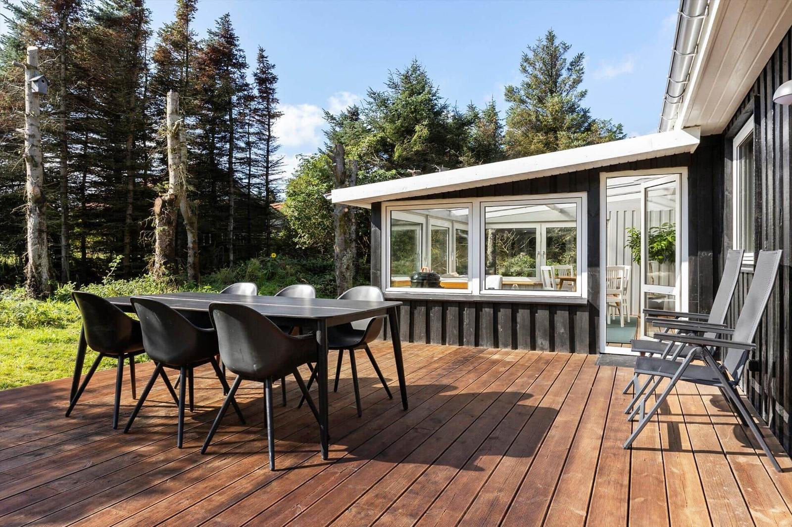 Deck with table and chairs, adjacent to a wooden cabin with glass front.