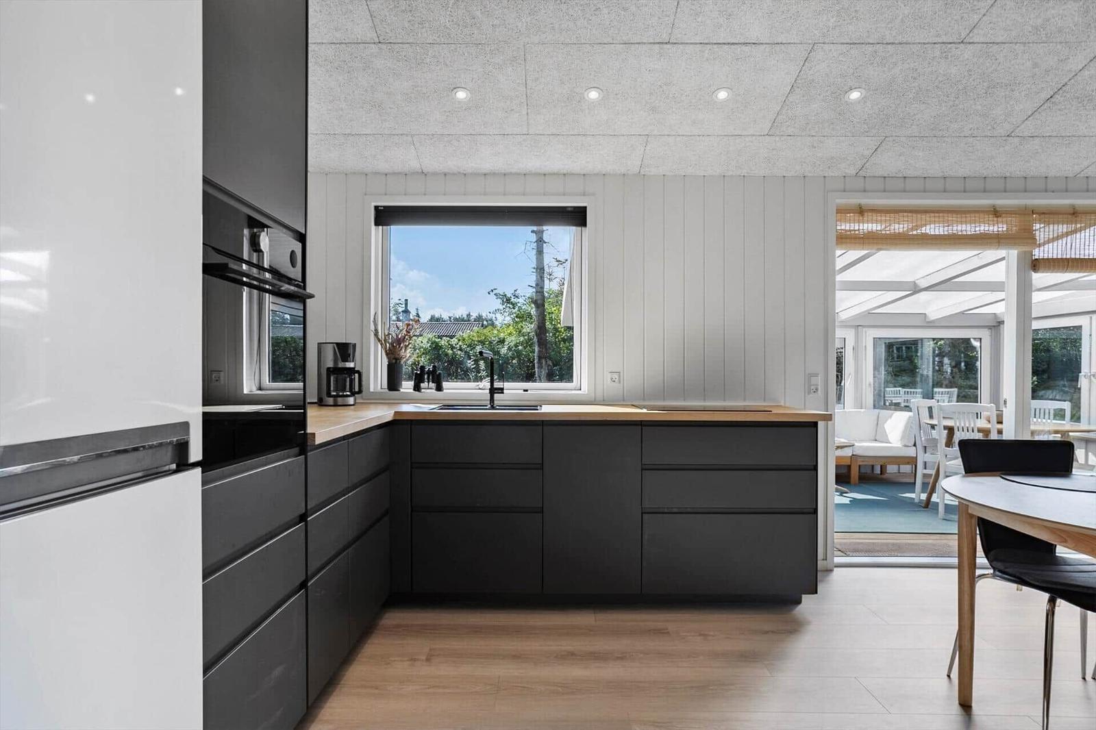 Kitchen with black cabinets, wooden countertop, and view of the garden.