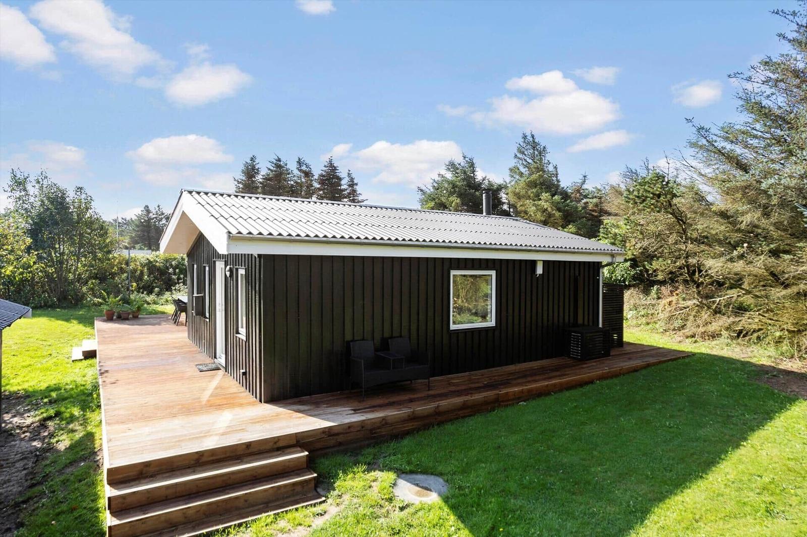 Wooden house with deck, garden, and tree view under blue sky.