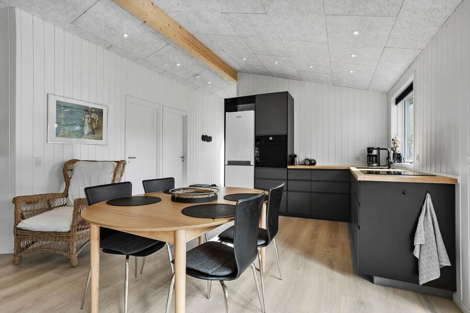 Kitchen with dining area, black cabinets, wooden table and chairs, wall art, and window.