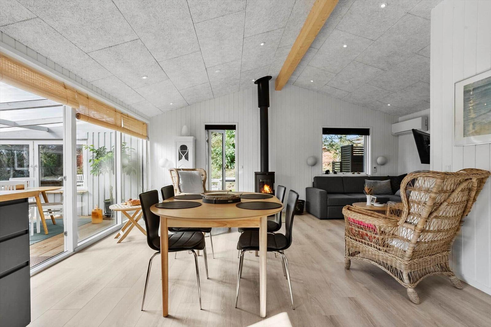 Dining area with table and chairs, living area with sofa and fireplace, large windows overlooking terrace.