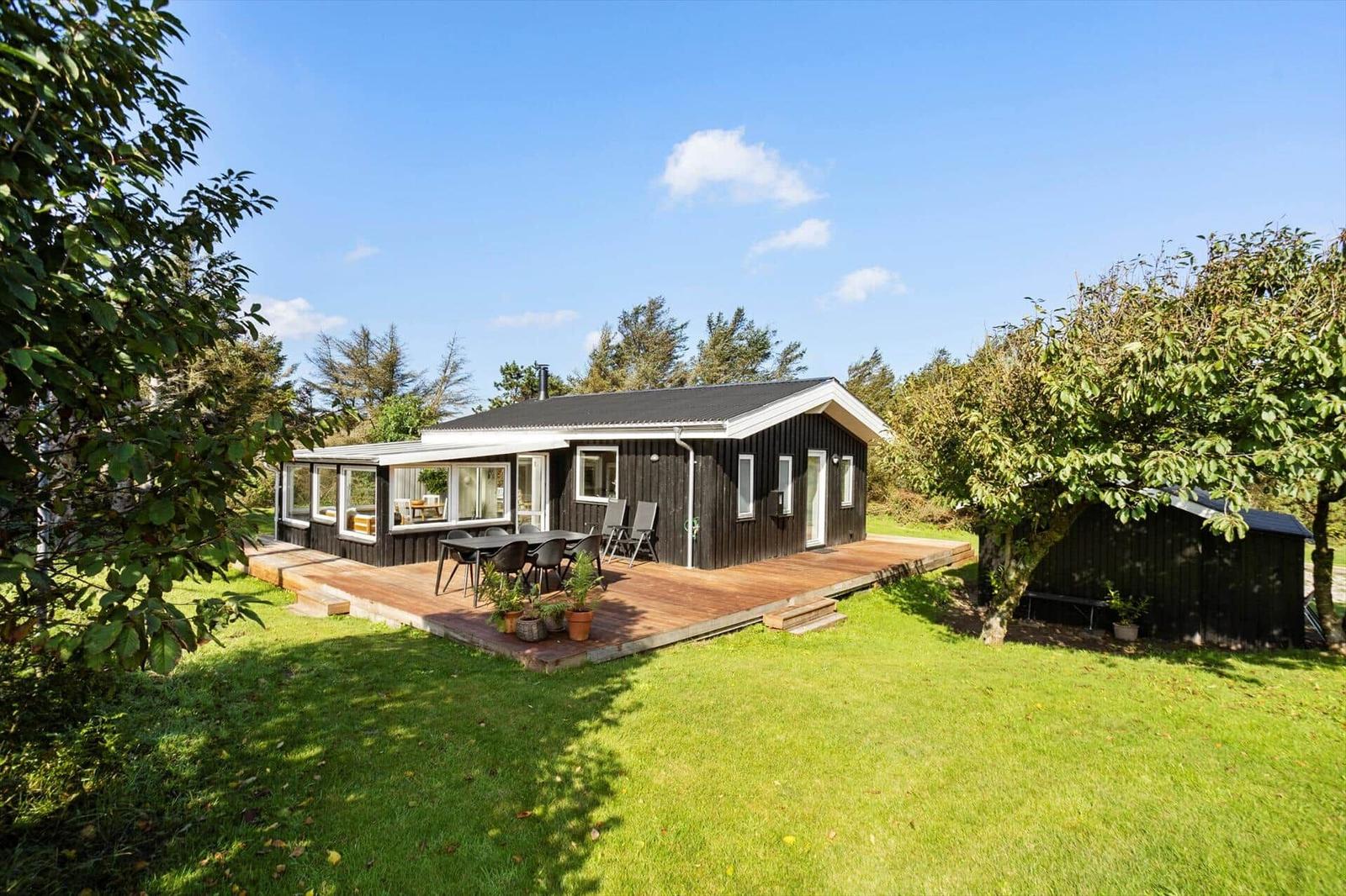 A black-clad house with a terrace and garden. Tables and chairs are outside.