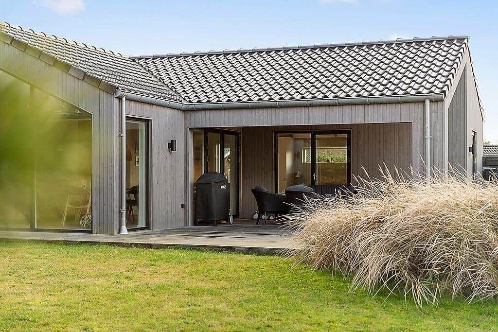 Modern villa with terrace, grill, and glass facades. Lawn and shrubs in the foreground.