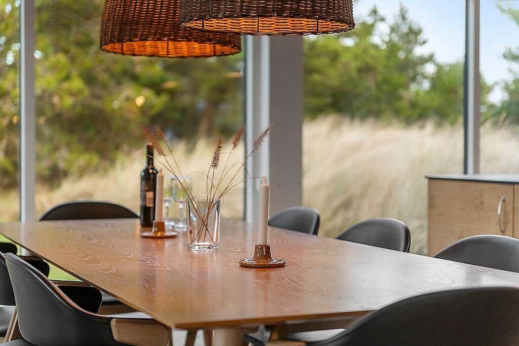 Dining table with chairs, candles, and wine by large window overlooking grass.