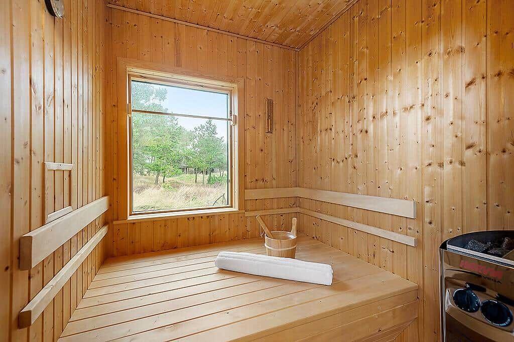 Wooden sauna with window, bucket, and bench.