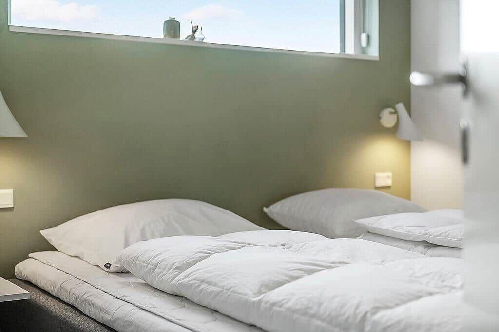 A bed with white pillows and a duvet. Two wall-mounted lamps are visible.