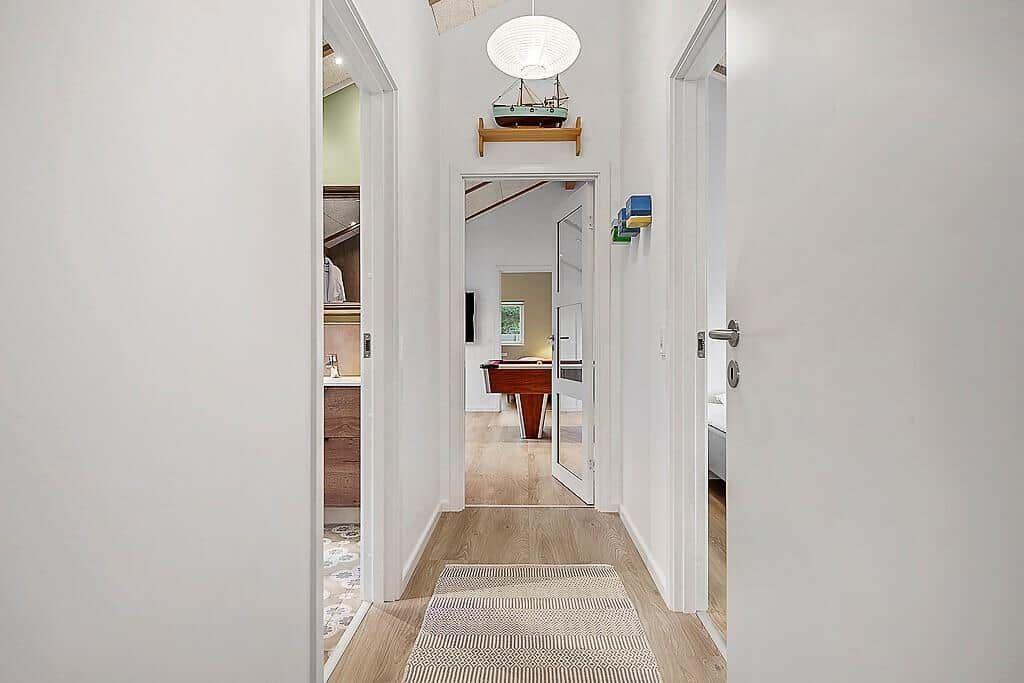 Hallway with wooden floor and rug, view into bedroom and game room with table.