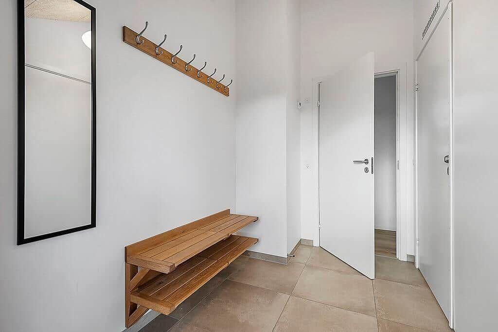 Entrance with wooden bench, mirror, and hook rack. White walls and door.