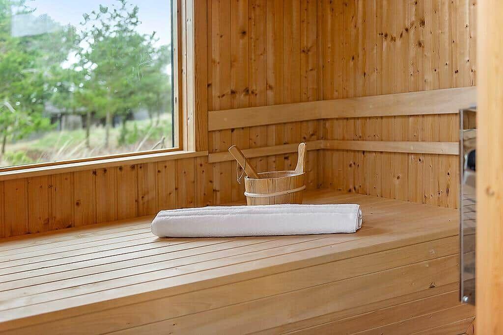 Sauna with wooden bench, white towel, and bucket with brush.