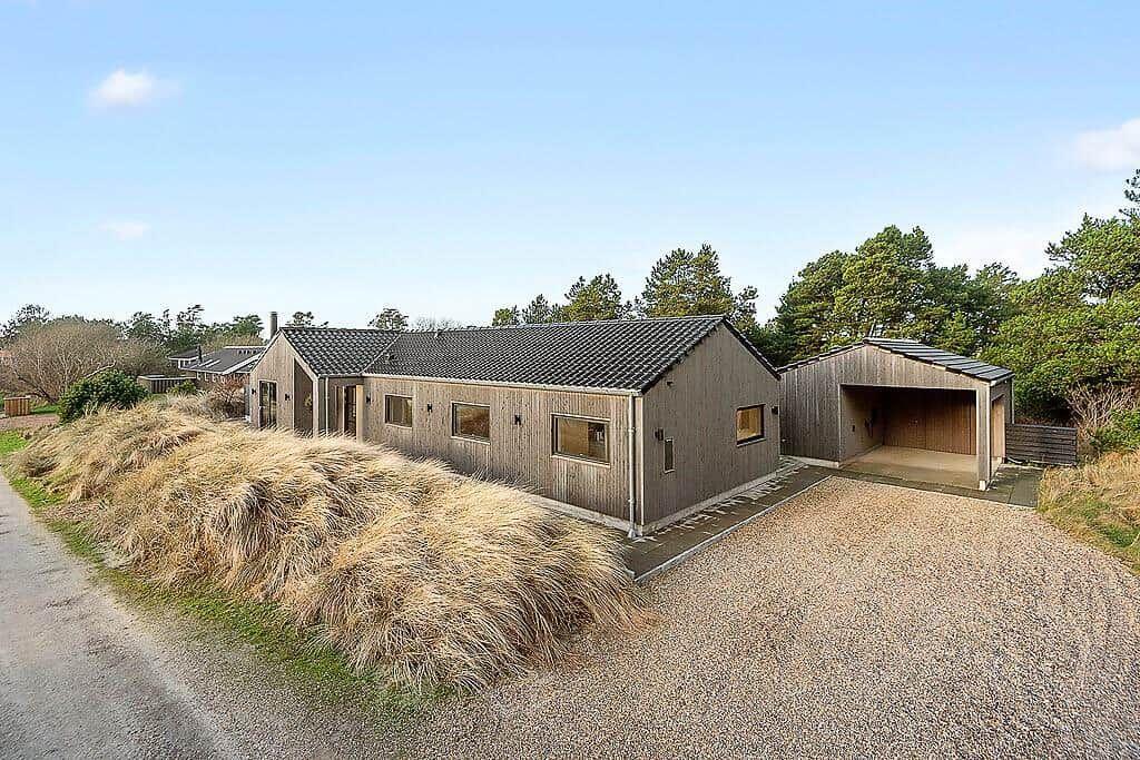 Modern wooden house with garage and grassy hill in the background.