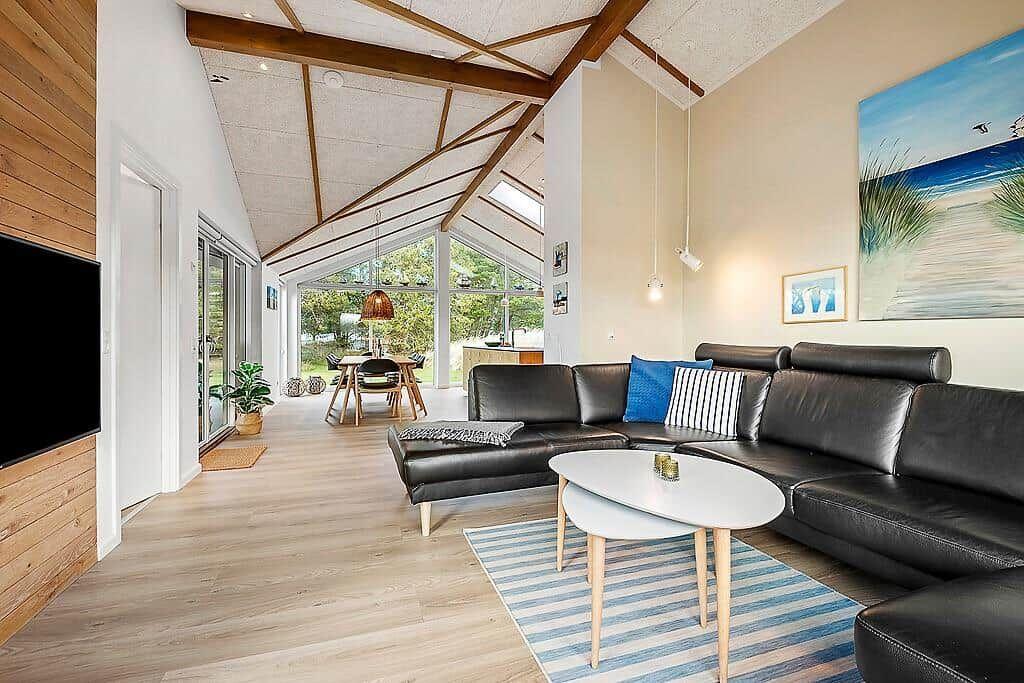 Living room with sofa, coffee table, and hardwood floor. Large windows and ceiling beams.
