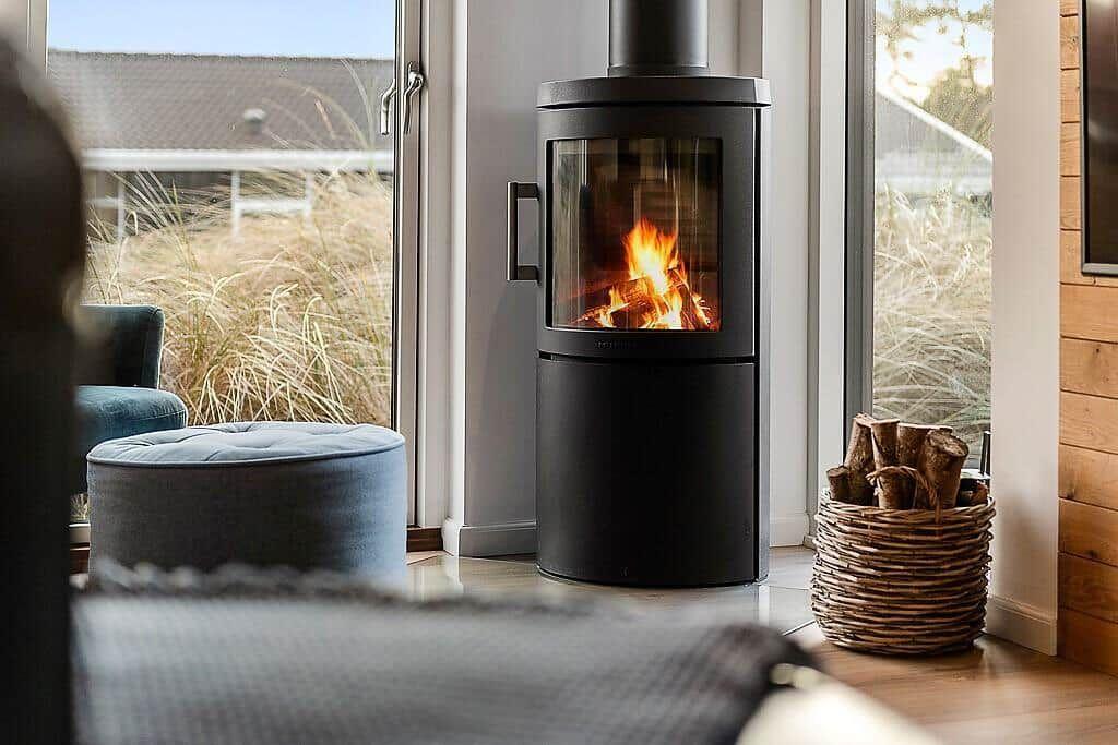 A black wood stove burns in the living room. Outside, tall grasses and a window are visible.