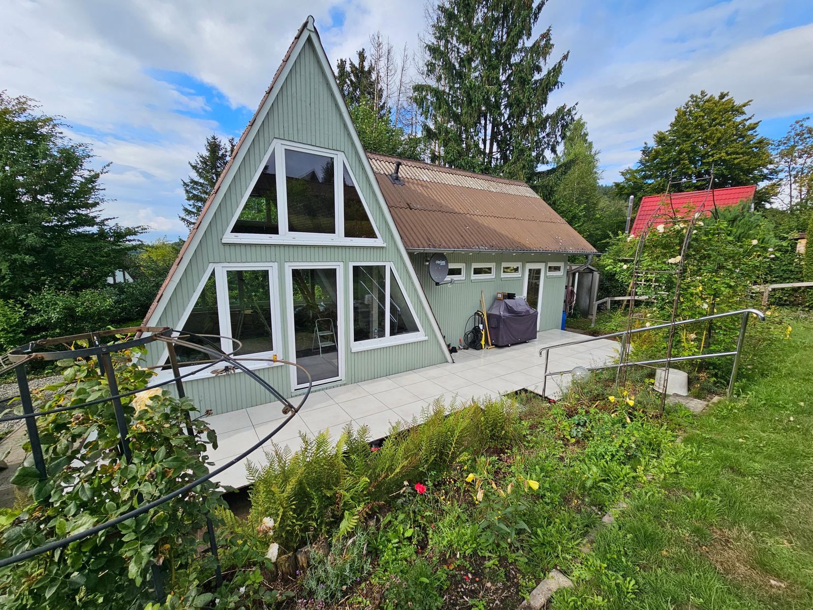 A-Frame-Haus mit Terrasse und Garten. Umgeben von Bäumen und Sträuchern.