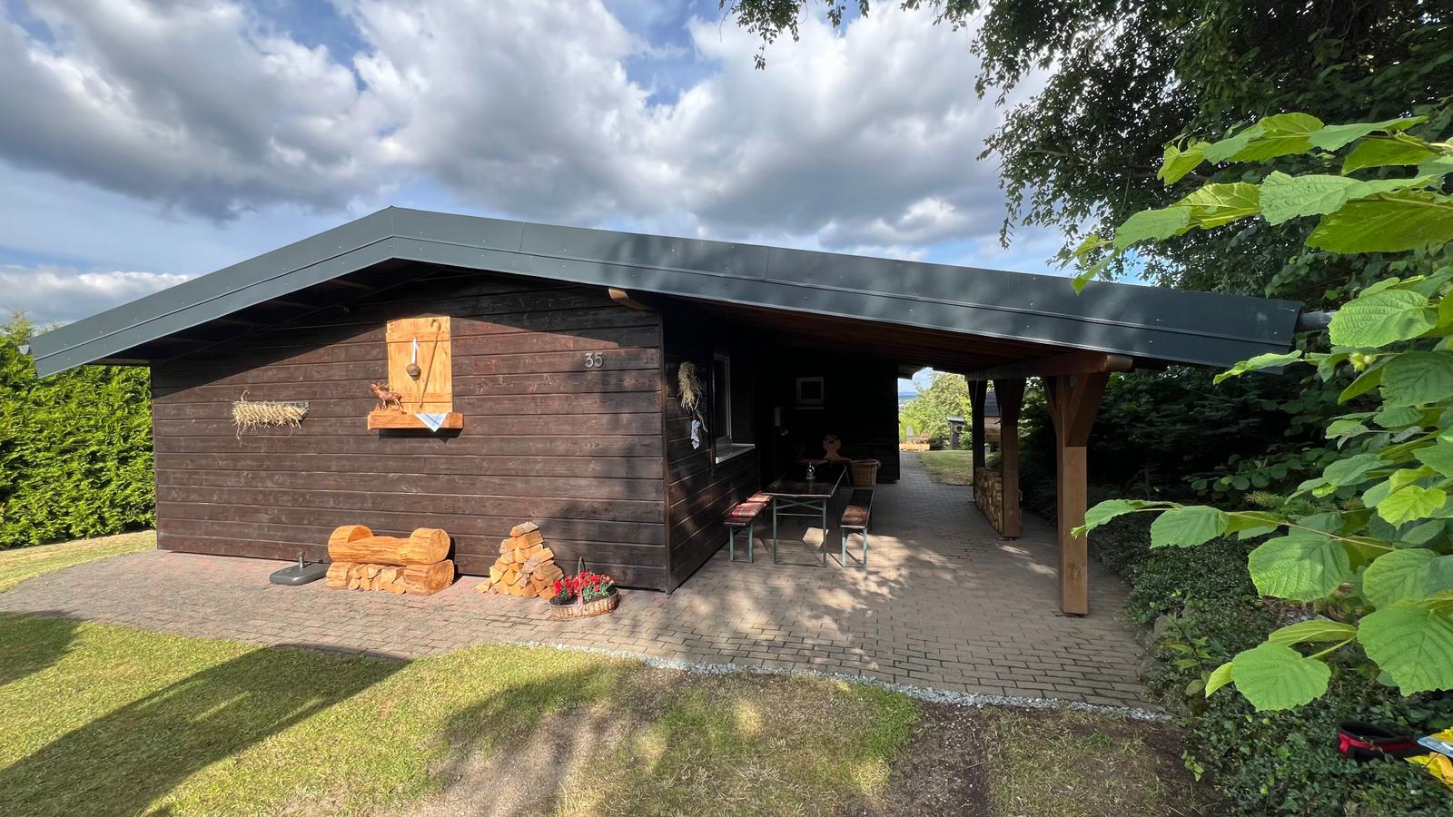 Holzhaus mit überdachter Terrasse, Grillplatz und Holzstapel.