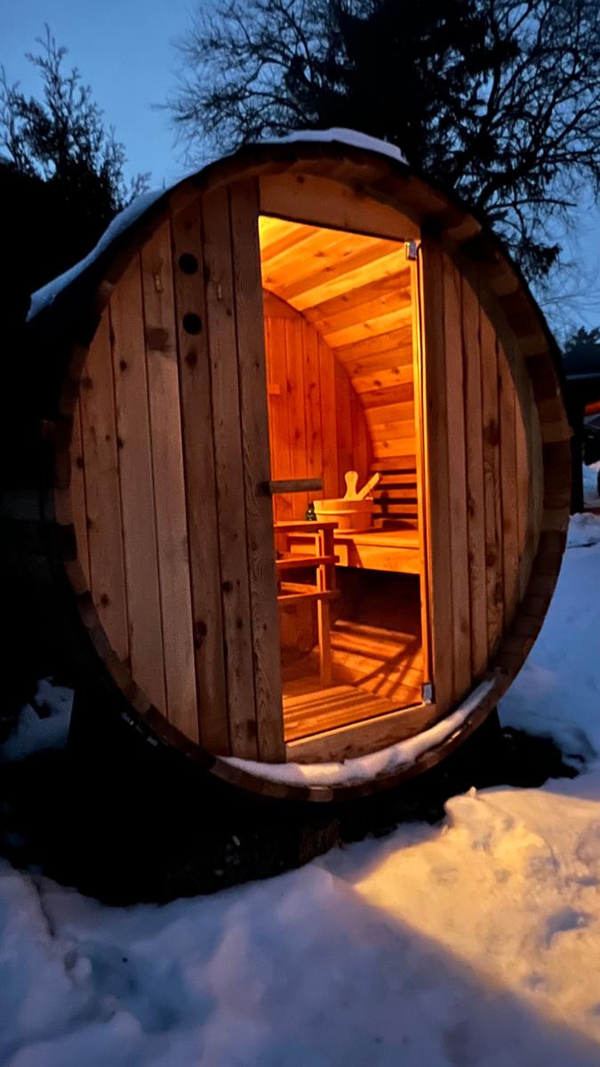 Holzsauna im Schnee mit geöffneter Tür und Sitzbänken im Inneren.