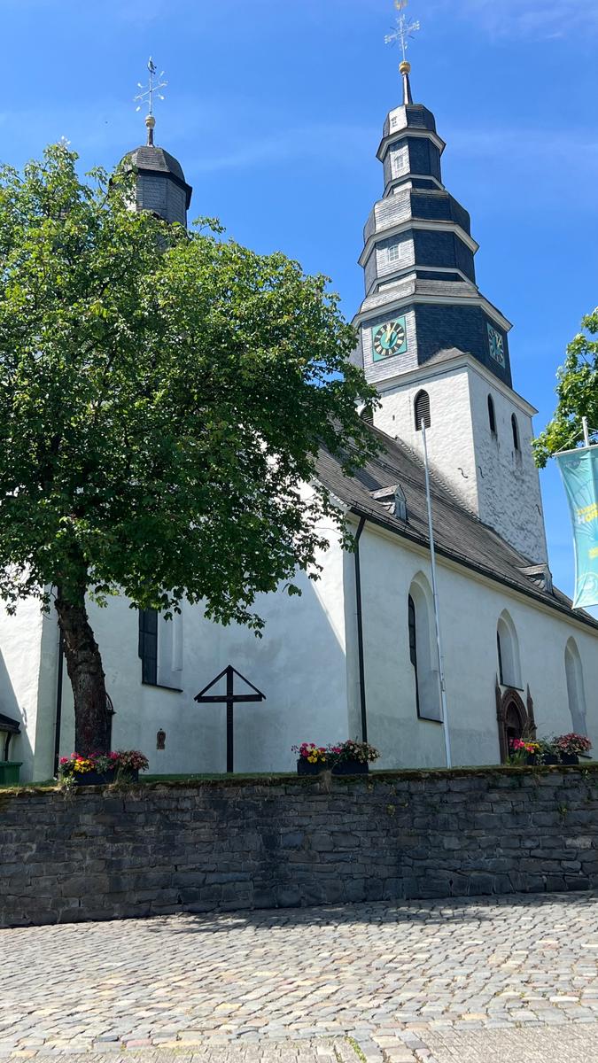 Historische Kirche mit Turm und Blumenbeeten vor Steinmauer.