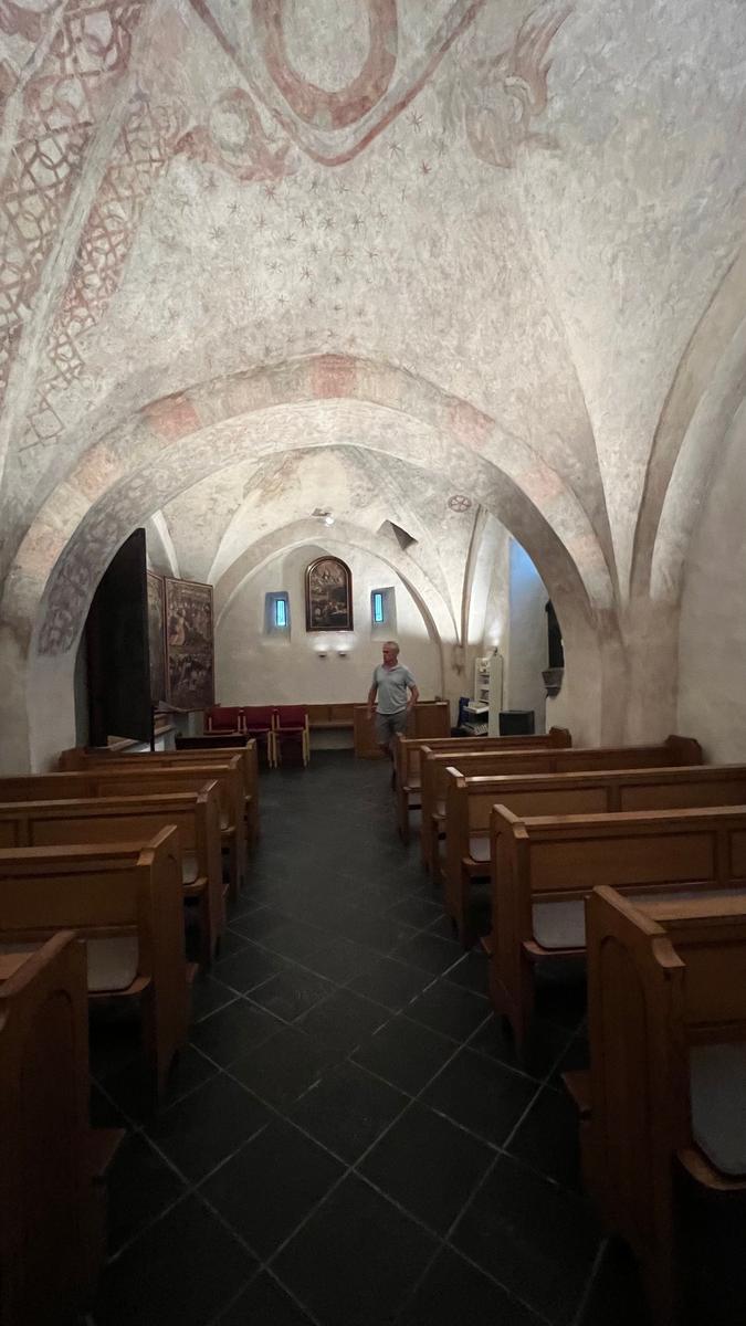 Innenraum einer Kirche mit Holzbänken, gemalten Decken und einem Altarbereich.