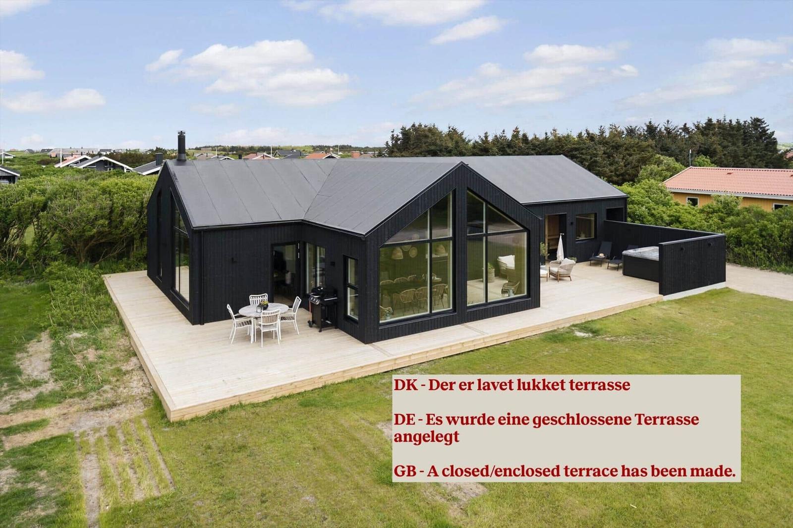 Moderne schwarze Villa mit großzügiger Terrasse und Sitzgelegenheiten.