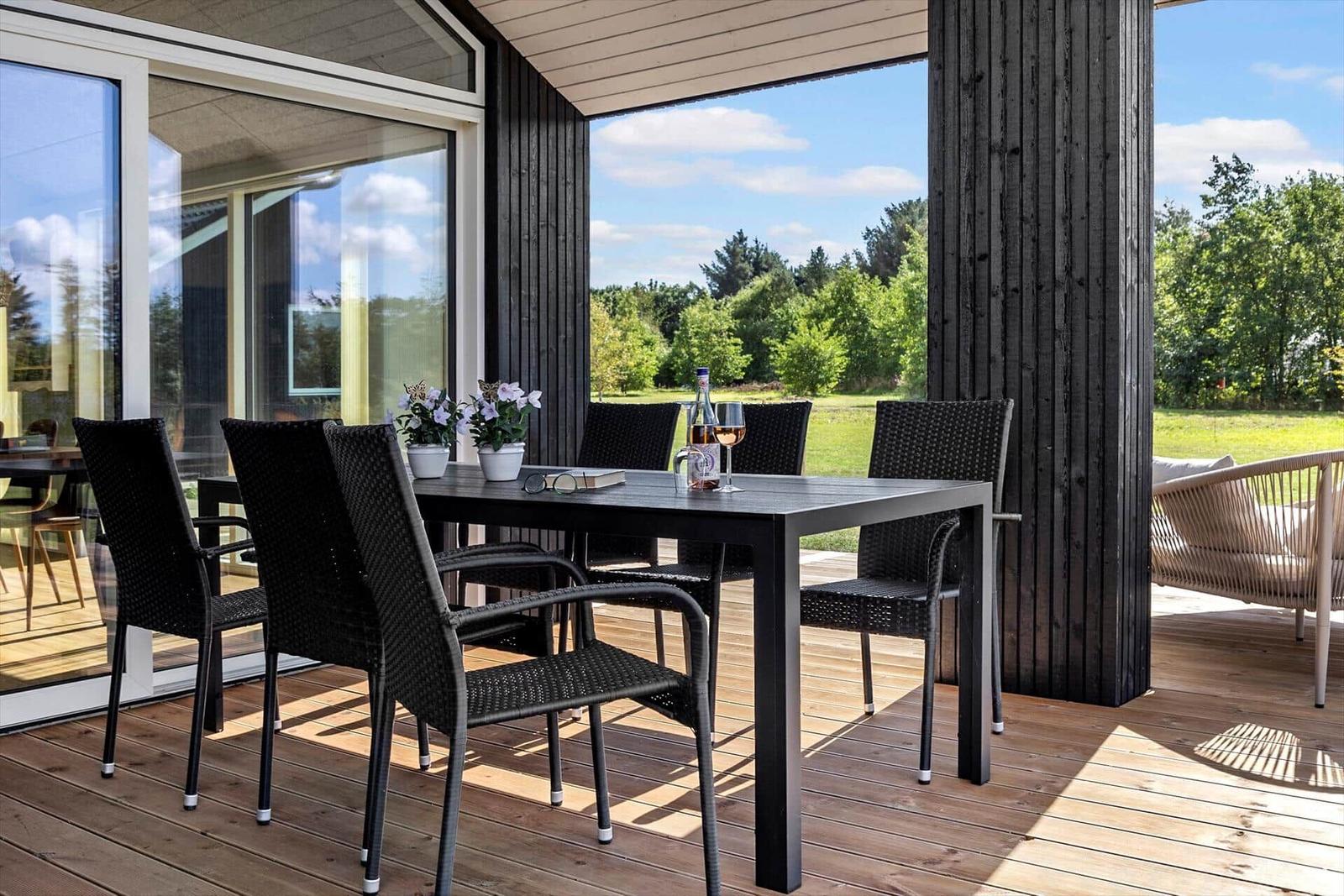 Terrasse mit Tisch und Stühlen, Blick auf Grünland und Bäume.
