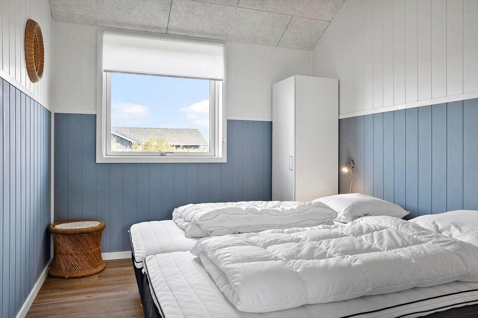 Schlafzimmer mit Bett, Fenster und Kleiderschrank. Wandverkleidung in Blau und Weiß.