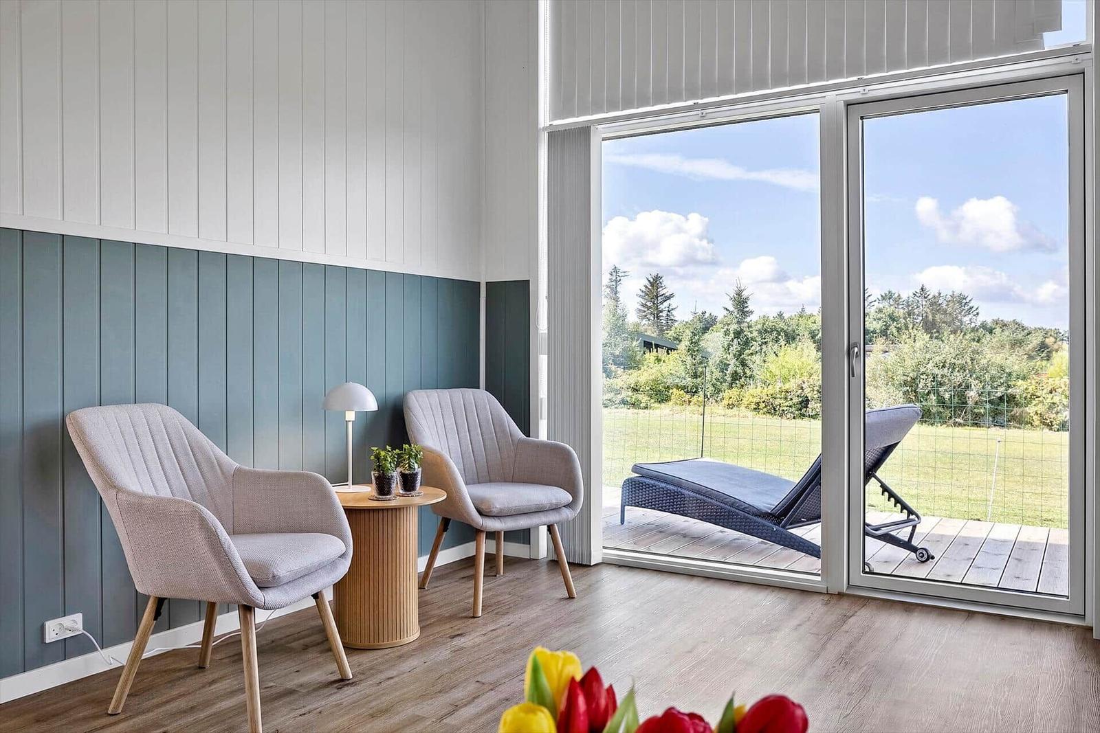 Zwei Stühle und Tisch stehen vor Fenster mit Blick auf Terrasse und Grün.